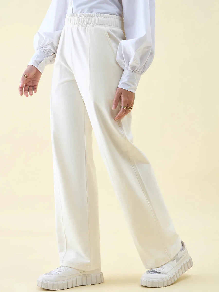 Person in 98degreenorth Butter Wide Leg Pintuck Trackpants, white sneakers, and a puffy-sleeve white blouse.