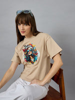 Woman in a 98degreenorth Casual Cotton Typography Print Tee, white pants, sunglasses on head, sitting on a wooden chair.