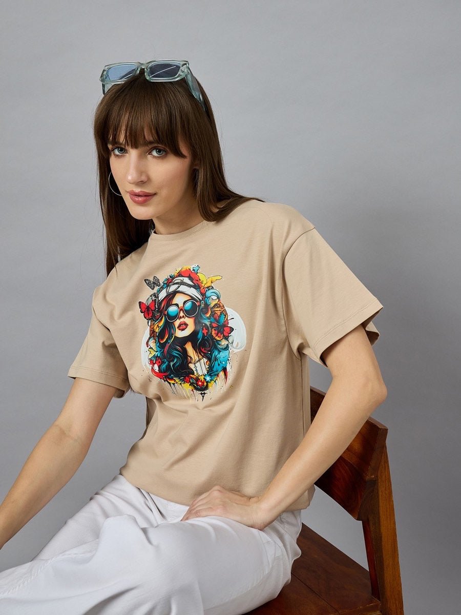 Woman in a 98degreenorth Casual Cotton Typography Print Tee, white pants, sunglasses on head, sitting on a wooden chair.