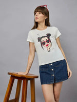 Woman in a 98degreenorth casual cotton typography t-shirt and denim skirt, leaning on a stool against a gray background.