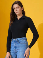 Woman in a 98degreenorth Classic Black Ribbed Polo-Neck Knit Top and blue jeans poses confidently against a yellow background.