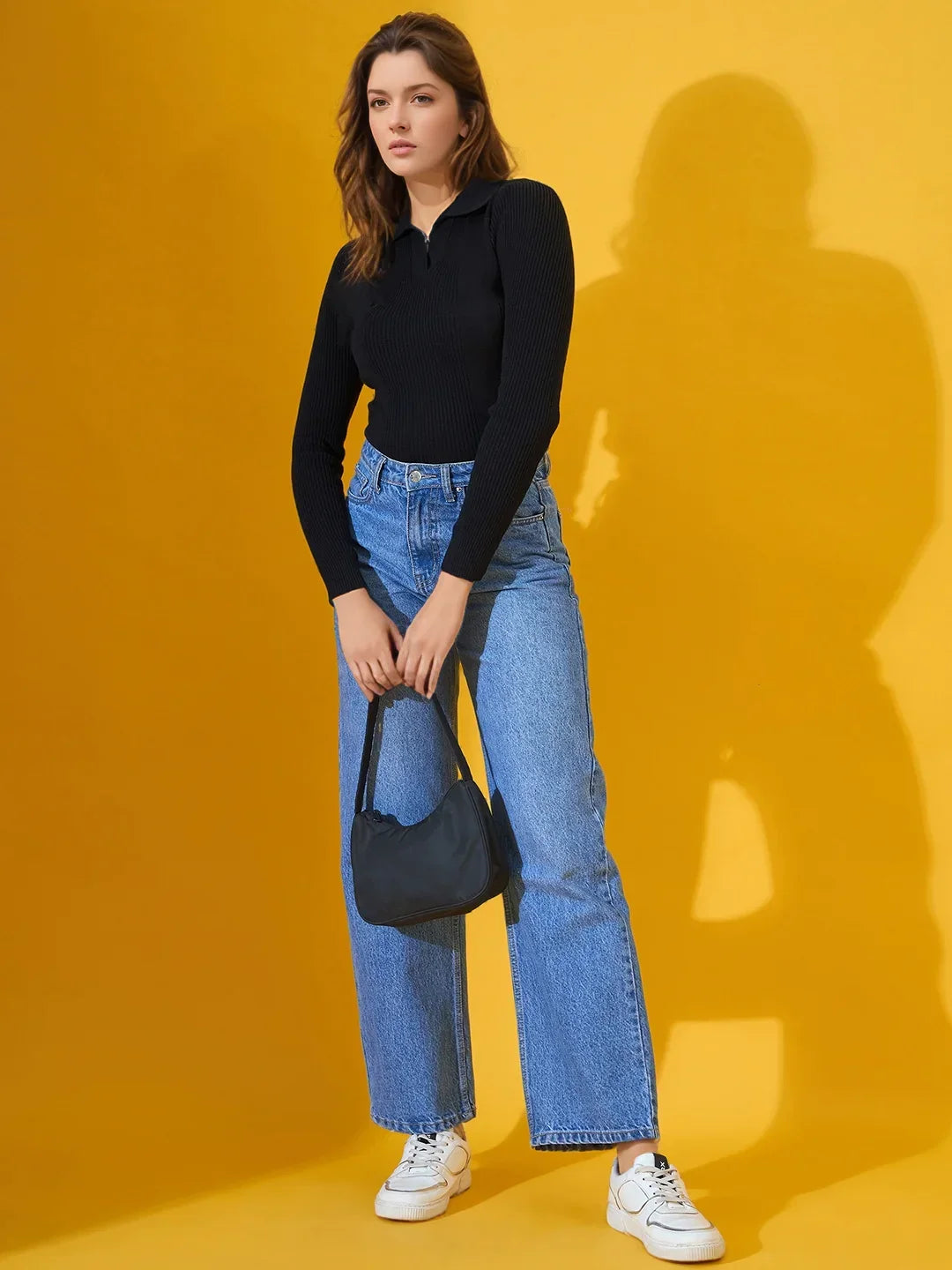 A woman in a black 98degreenorth Classic Ribbed Polo-Neck Top, blue jeans, white sneakers, and holding a navy bag.