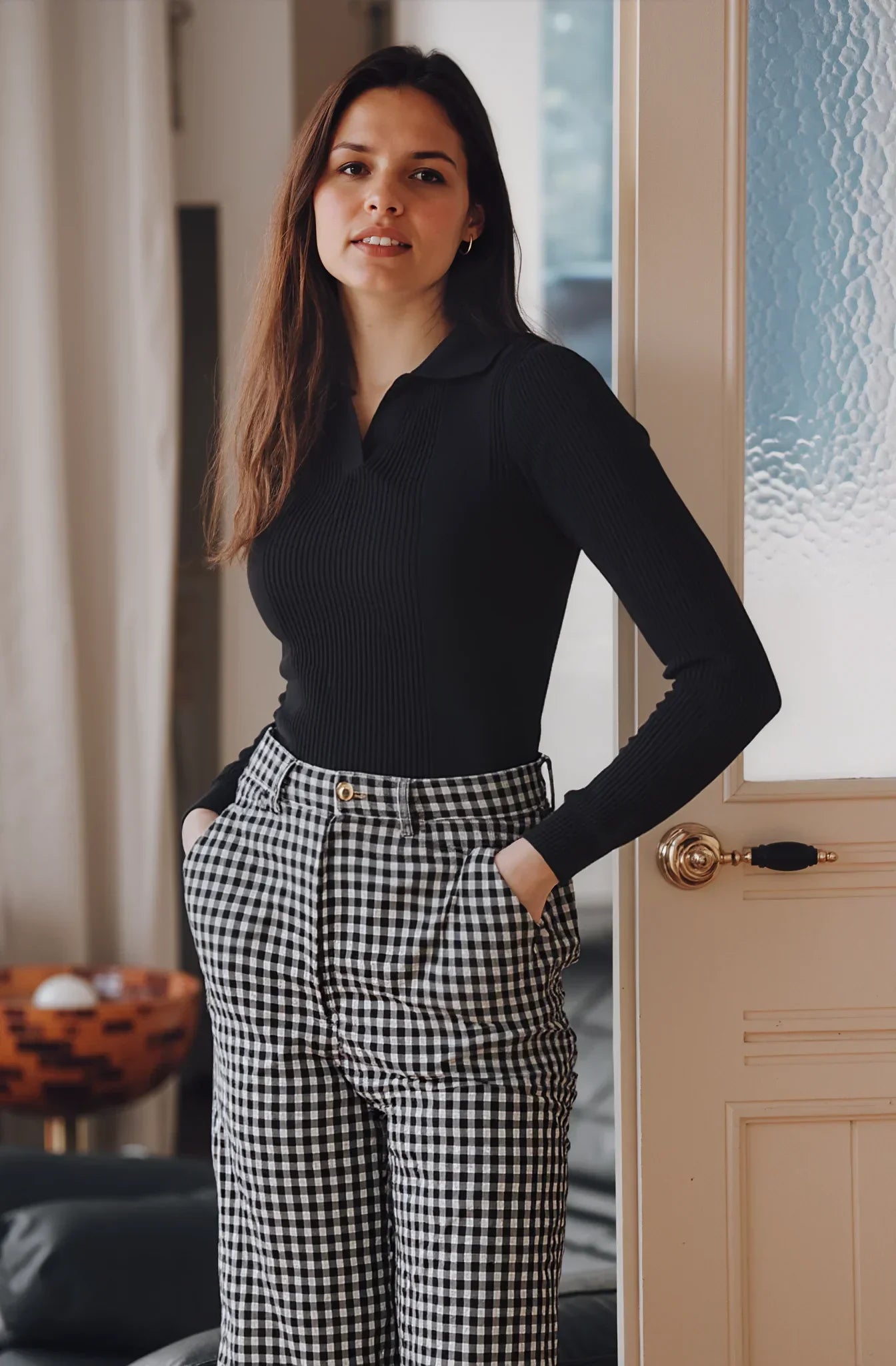 Woman wears 98degreenorth Classic Black Ribbed Polo-Neck Knit Top, hands in pockets, looking at the camera.