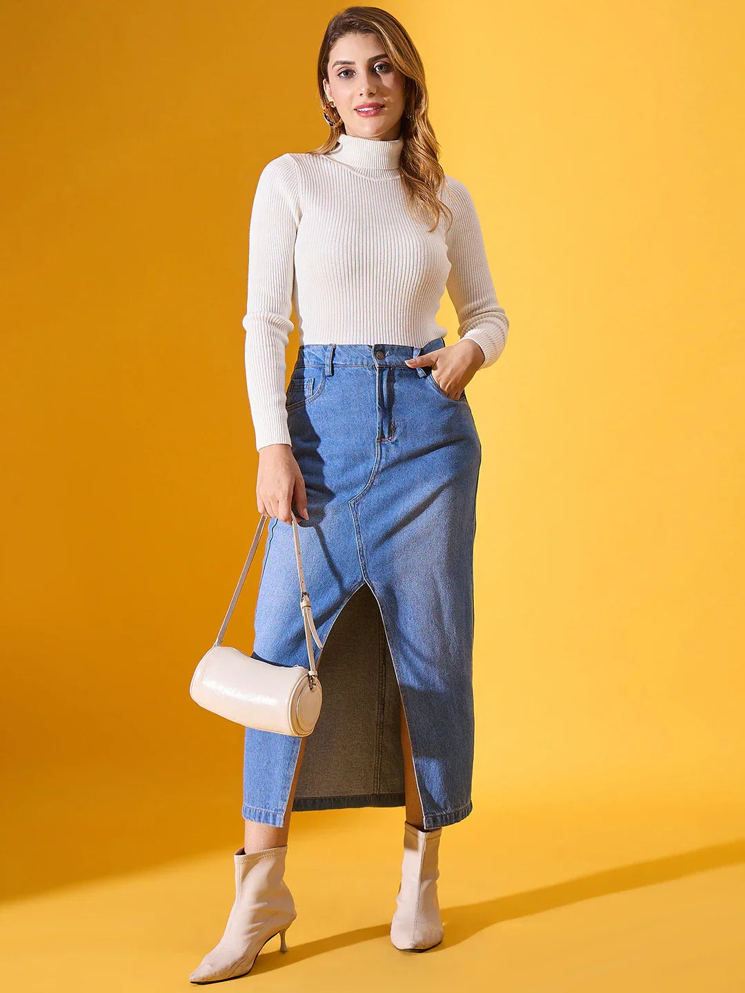 Woman wears 98degreenorth Classic White Ribbed Stretchable Turtleneck Sweater, denim skirt, and beige boots in India.