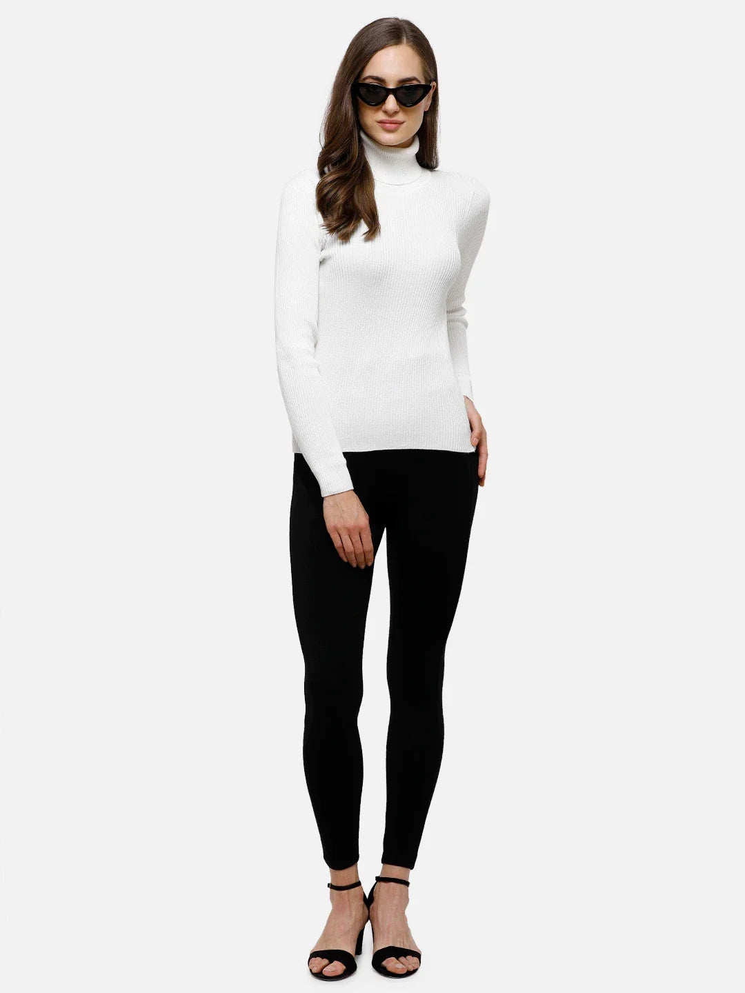 Woman in 98degreenorth Classic White Ribbed Turtle Neck Sweater, black leggings, sunglasses & sandals vs. plain backdrop.
