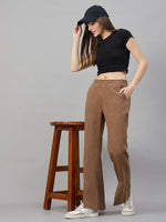 Woman in 98degreenorth Coffee Melange Fleece Bootcut Sweatpants poses by a wooden stool against a plain gray background.