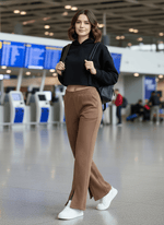 A woman in a black hoodie and 98degreenorth Coffee Melange Women’s Fleece Bootcut Sweatpants smiles at the airport.