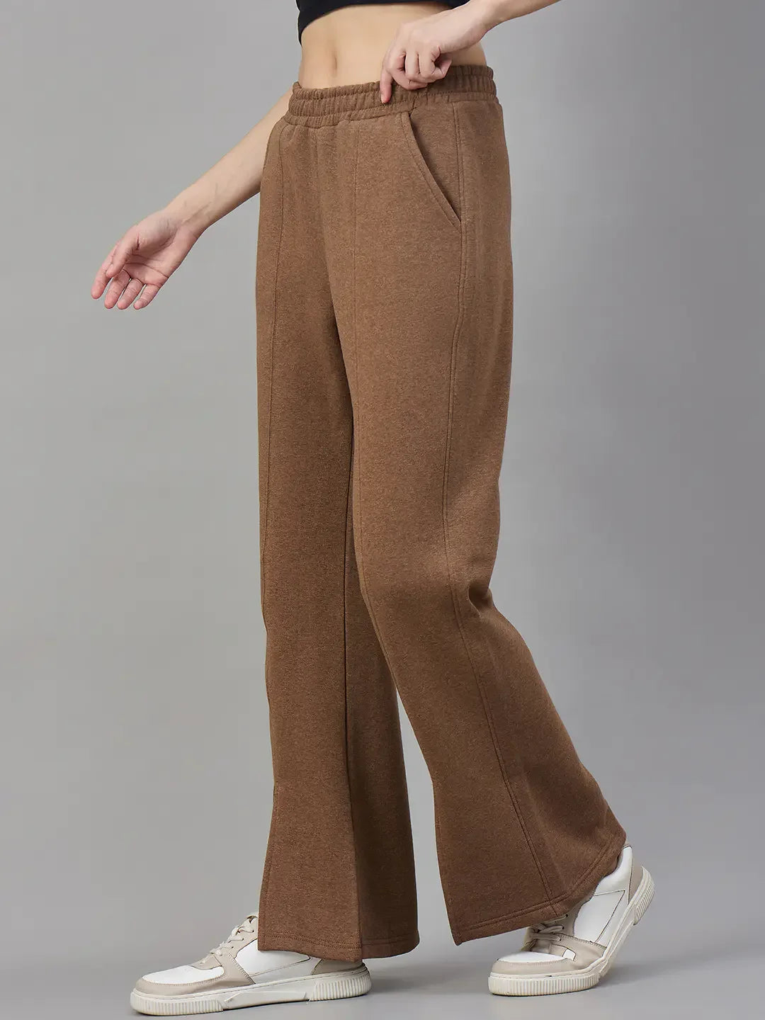 Model in 98degreenorth Coffee Melange Women’s Fleece Bootcut Sweatpants and white sneakers, against a grey backdrop.