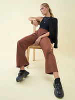 Woman in a black top, blazer, and 98degreenorth Dark Rust Wide Leg Pintuck Trackpants sits casually on a beige chair.