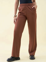 Person in 98degreenorth Dark Rust Wide Leg Pintuck Trackpants, black top, chunky shoes, and gold bangles, hands in pockets.
