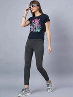 Woman in a 98degreenorth soft cotton typography t-shirt, gray leggings, silver sneakers, and white sunglasses poses.