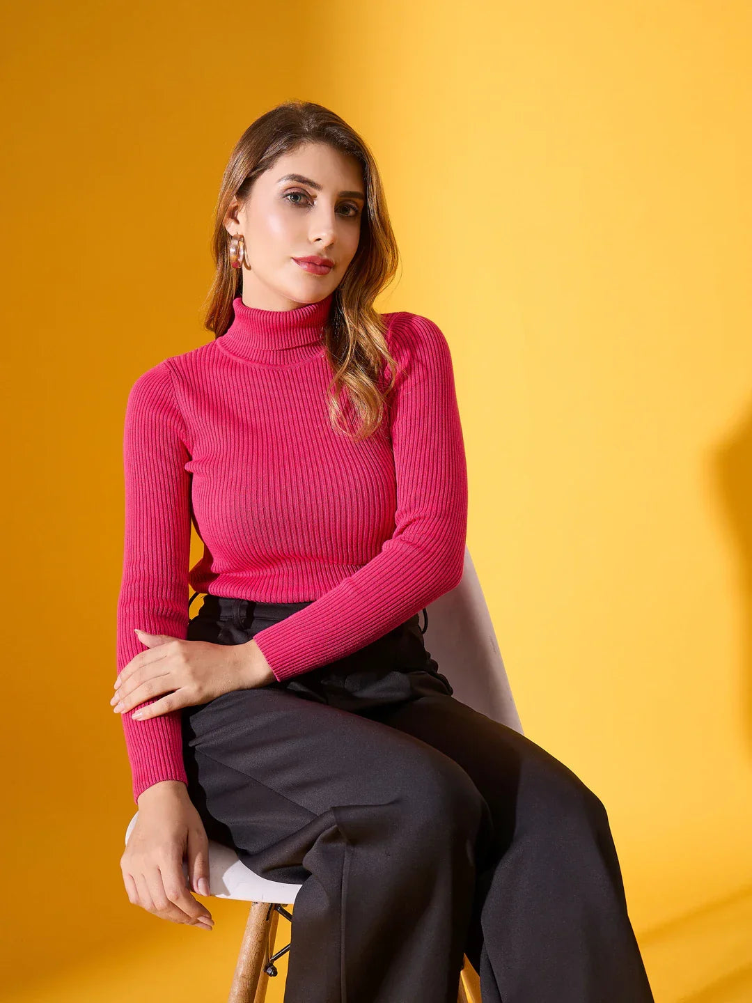 A woman wears the 98degreenorth Fuchsia Women’s Ribbed Stretch Turtleneck Sweater, seated against a yellow background.