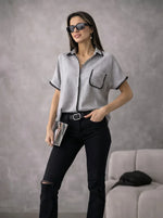 Woman in sunglasses wearing a Grey Whipstitch Trim Cotton Shirt by 98degreenorth, holding a clutch near a gray sofa.