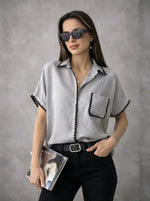 Woman in sunglasses wears the Grey Whipstitch Trim Cotton Shirt by 98degreenorth, holding a magazine against a gray backdrop.