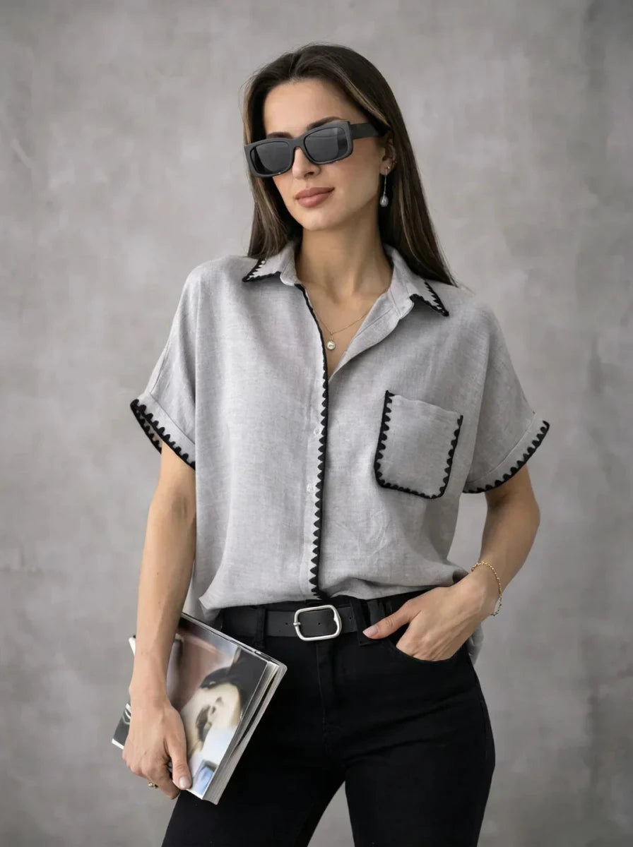 Woman in sunglasses wears the Grey Whipstitch Trim Cotton Shirt by 98degreenorth, holding a magazine against a gray backdrop.