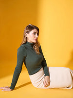 Woman in a 98degreenorth Hunter Green Ribbed Turtleneck Sweater and cream skirt sits on a yellow floor, looking aside.