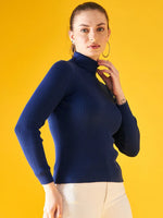 Woman wears the 98degreenorth Indigo Ribbed Knit Turtleneck Sweater, a slim fit pullover, with white pants.