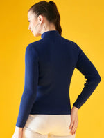 Woman wears 98degreenorth Indigo Ribbed Knit Turtleneck Sweater, slim fit stretch pullover, facing away on yellow.