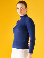 Woman models 98degreenorth Indigo Ribbed Knit Turtleneck Sweater against a bright yellow backdrop.