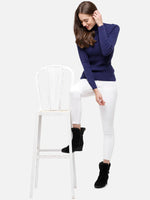Woman in 98degreenorth's ink blue ribbed slim fit turtleneck sweater poses, smiling, with one leg on a white chair.