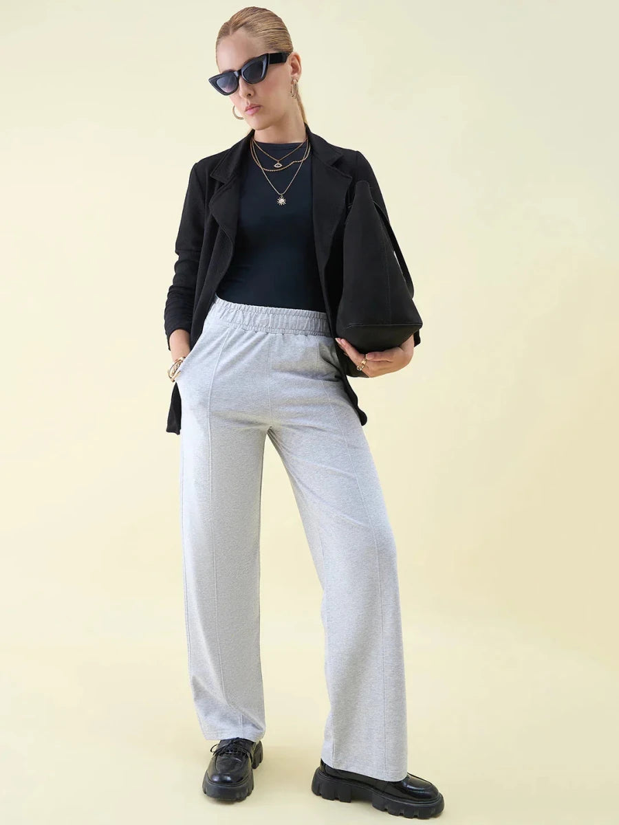 Woman in sunglasses and layered necklaces wears 98degreenorth Luxe Lounge Light Grey Wide Leg Pintuck Trackpants.