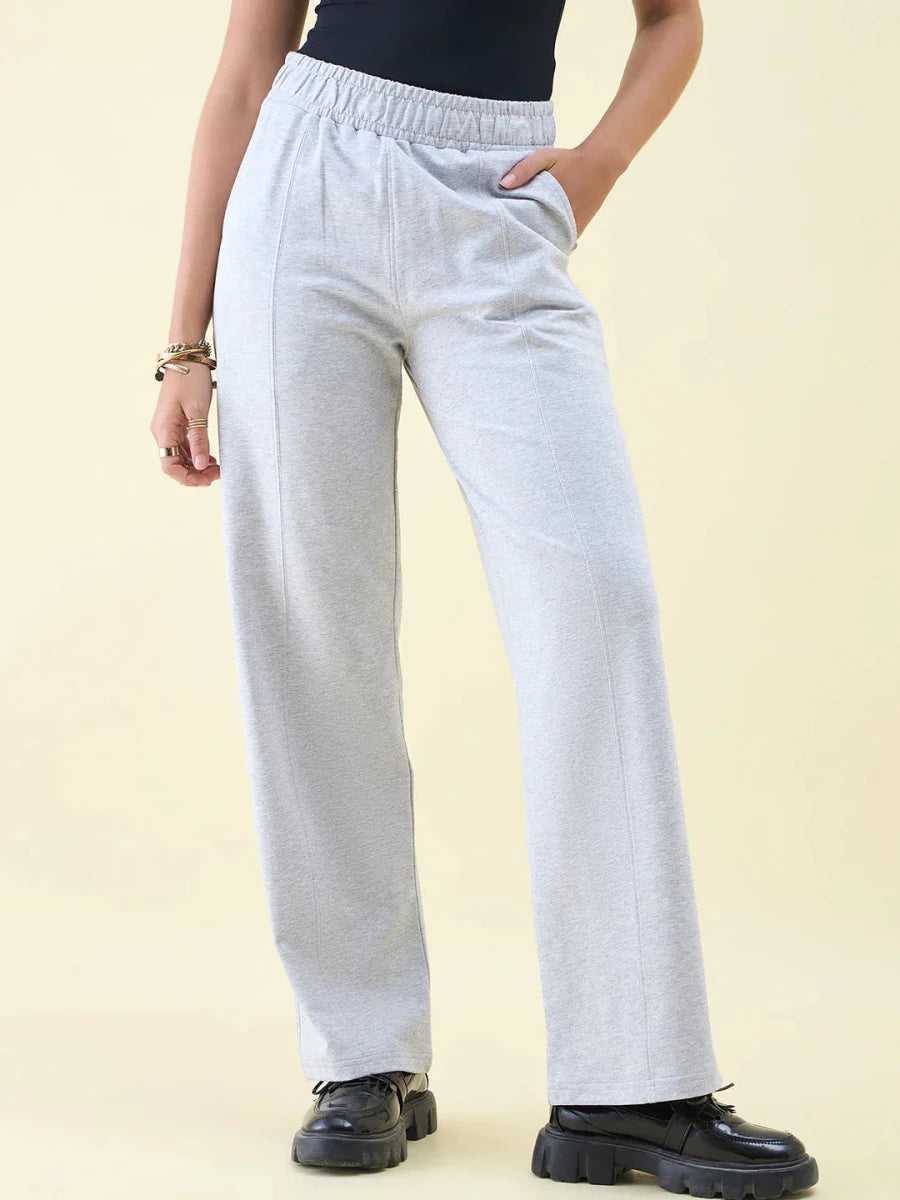 Person in 98degreenorth Light Grey Wide Leg Pintuck Trackpants, black top, and chunky shoes against a beige backdrop.
