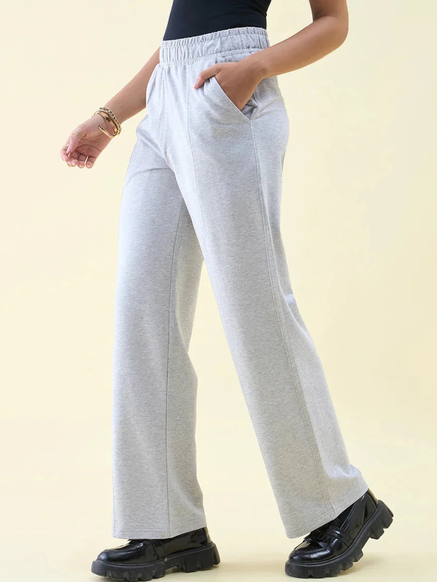 Person wearing 98degreenorth Light Grey Wide Leg Pintuck Trackpants, black top, black shoes, bracelets, hands in pockets.