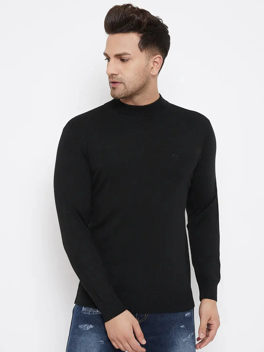 A man with short, styled hair wears the 98degreenorth Men Merino Wool Black Turtleneck Pullover and blue distressed jeans, standing against a white background and looking left with a neutral expression.