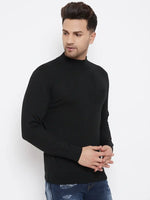 A man wearing a 98degreenorth Men Merino Wool Black Turtleneck Pullover and distressed blue jeans stands against a plain white background, looking to his left with his hands lightly clasped in front of him.