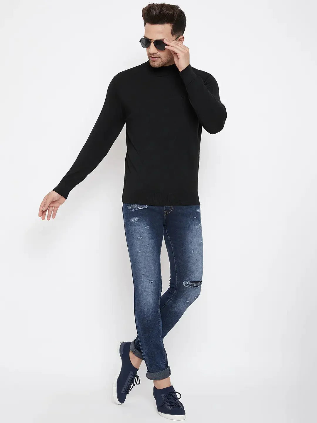 A man in a 98degreenorth Men Merino Wool Black Turtleneck Pullover, blue distressed jeans, blue sneakers, and sunglasses poses stylishly against a plain white background.