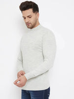 A man with short dark hair wears the 98degreenorth Men Merino Wool Ecru Turtleneck Pullover and dark blue jeans, standing against a white background with his hands gently clasped as he looks down.