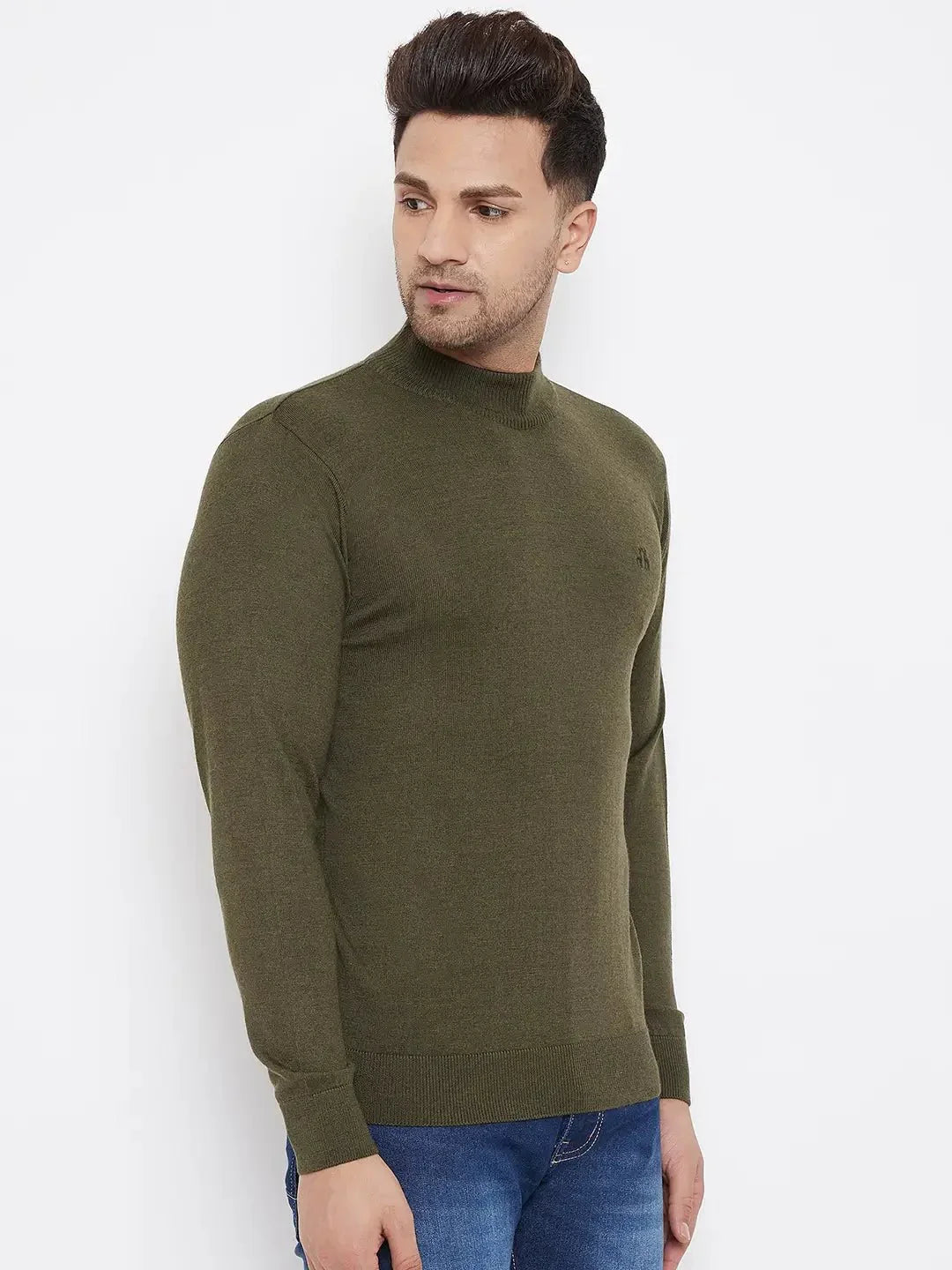 A man with short, styled hair wears an olive Men Merino Wool Turtleneck Pullover by 98degreenorth and blue jeans, standing against a white background and looking to his left.