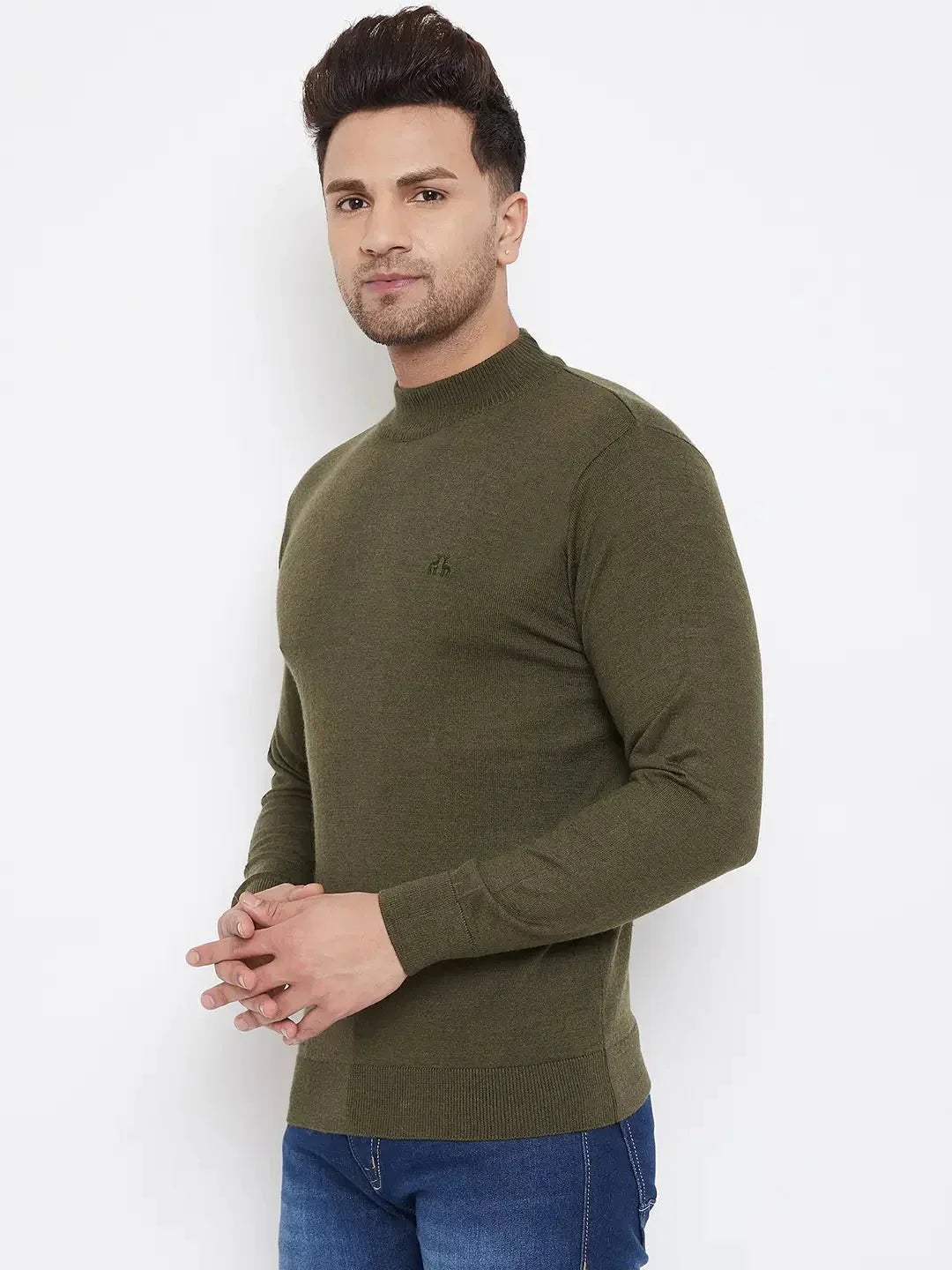 A man in a 98degreenorth Men Merino Wool Olive Turtleneck Pullover and blue jeans stands against a white background, facing the camera with his hands clasped in front.