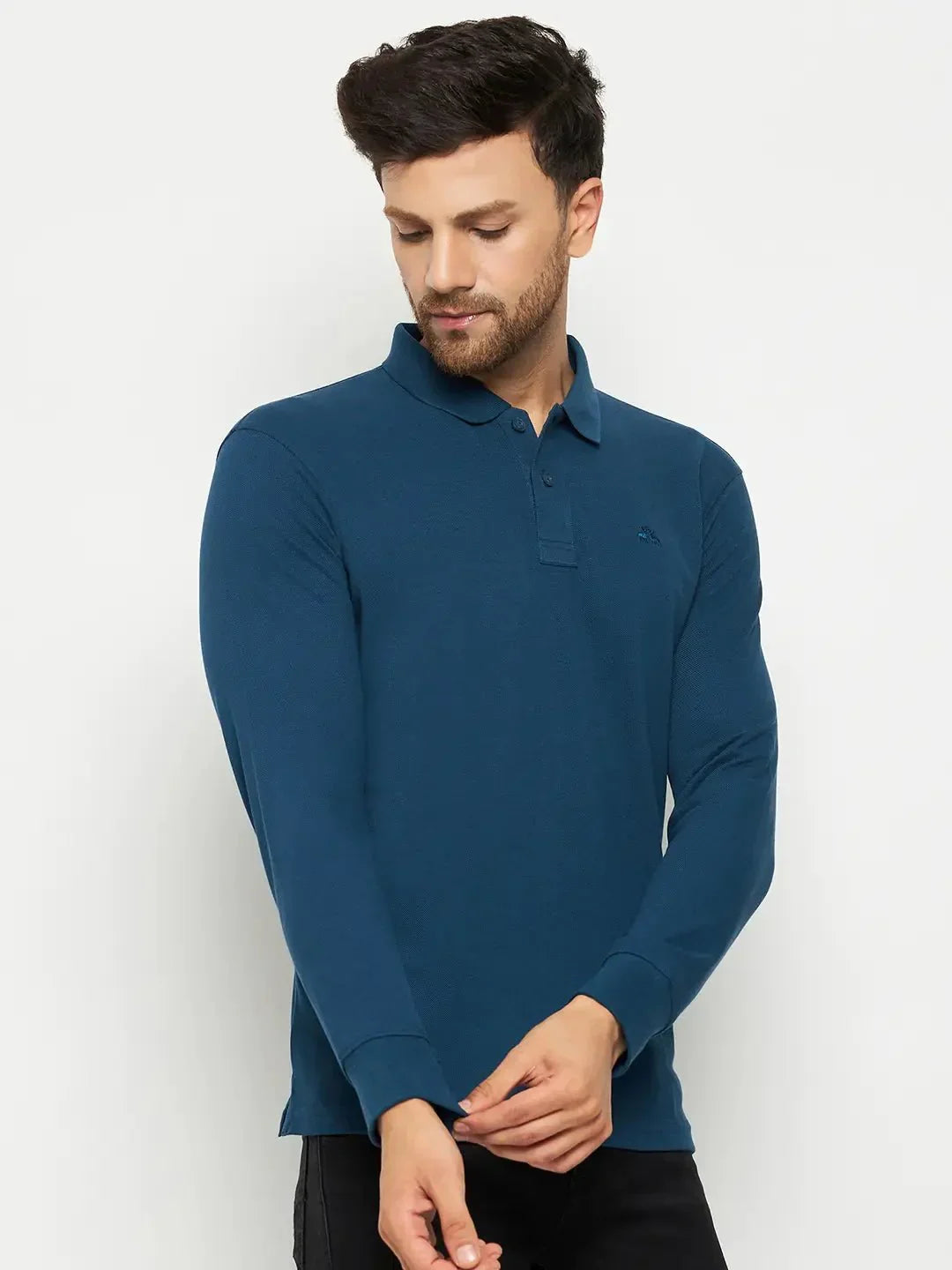 Man in a 98degreenorth Men Polo Collar Full Sleeves Teal T-shirt, adjusting his sleeve against a plain background.
