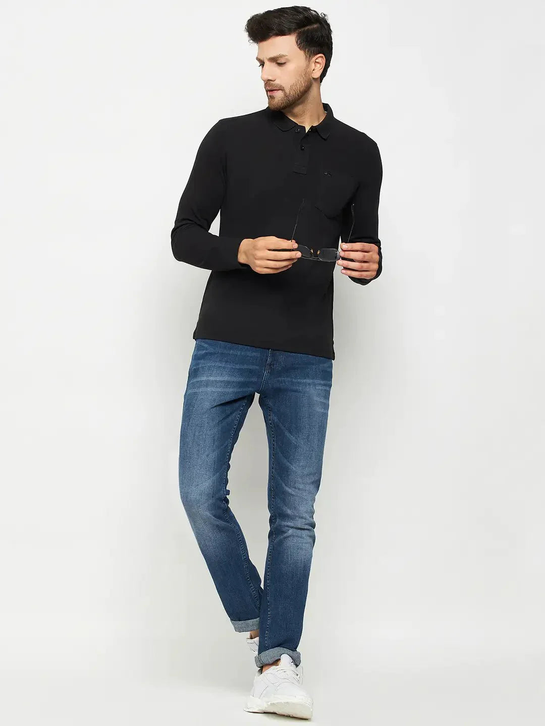 Man in a 98degreenorth Men Polo Collar Full Sleeves With Pocket Black T-shirt, blue jeans, and white sneakers holding sunglasses.