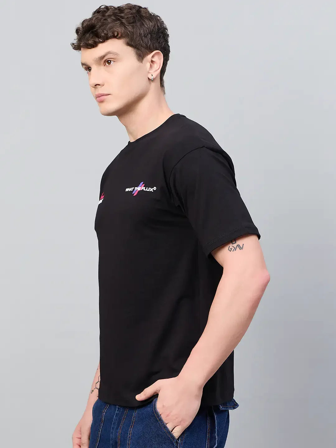 Man in a 98degreenorth Men Typography Black Printed Round Neck T-shirt stands sideways, hands in pockets, on gray background.