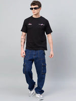 Man in sunglasses wears a 98degreenorth Men Typography Black Printed Round Neck T-shirt, blue cargo jeans, and gray sneakers.