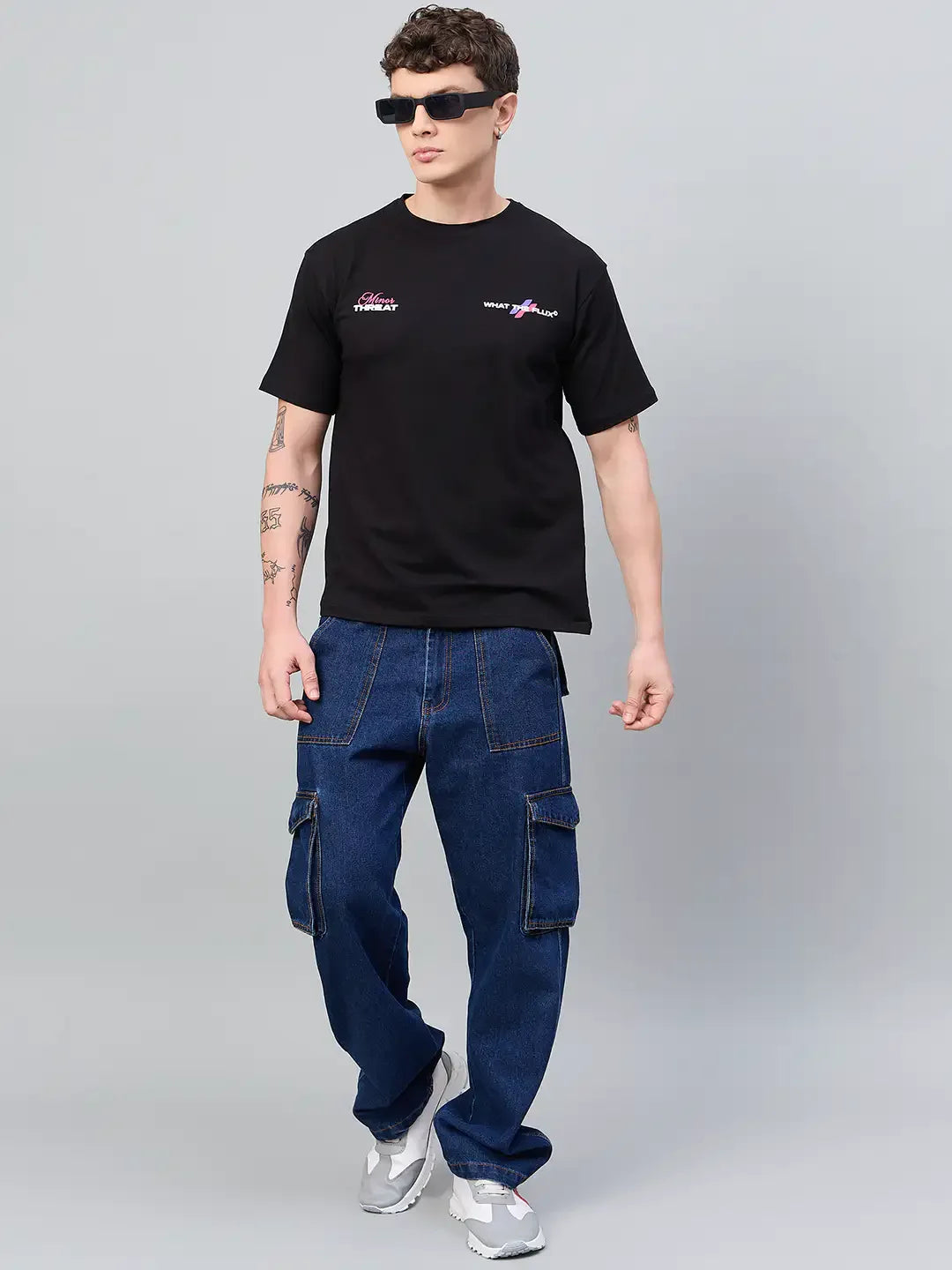 Man in sunglasses wears a 98degreenorth Men Typography Black Printed Round Neck T-shirt, blue cargo jeans, and gray sneakers.