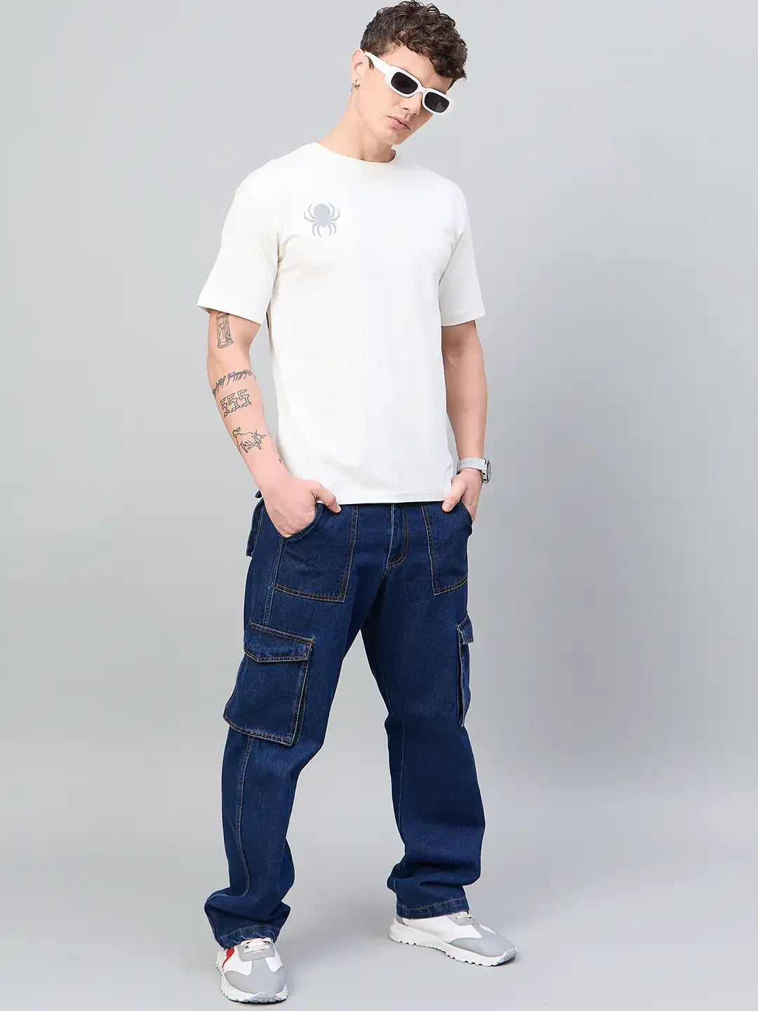 Man wears 98degreenorth Men Typography Offwhite Printed Round Neck T-shirt, blue cargos, white sneakers, and shades.