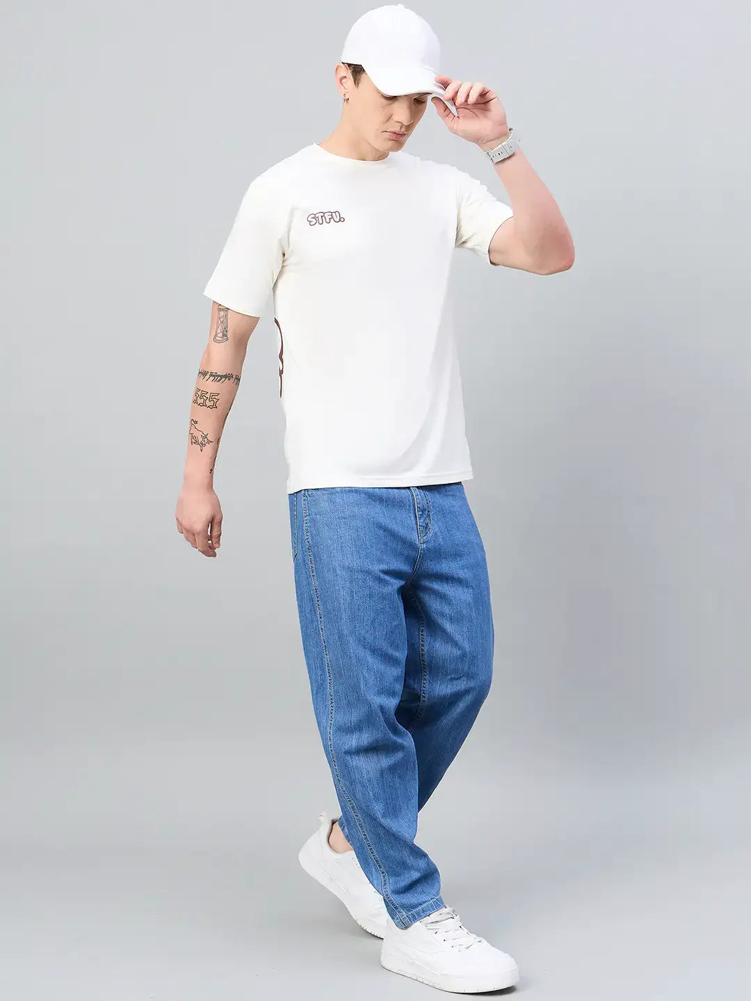 Man wears 98degreenorth Men Typography Oversized Offwhite Printed T-shirt, blue jeans, white cap, and sneakers.