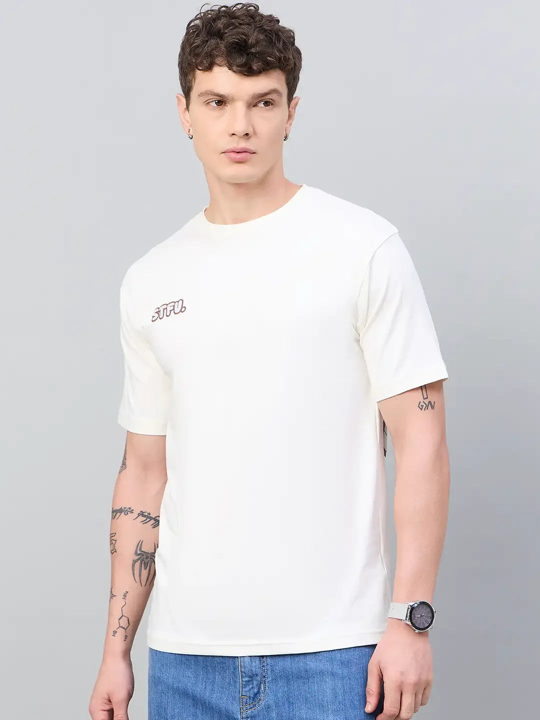 Man with short curly hair wears 98degreenorth Men Typography Oversized Offwhite Printed T-shirt, blue jeans, wristwatch.