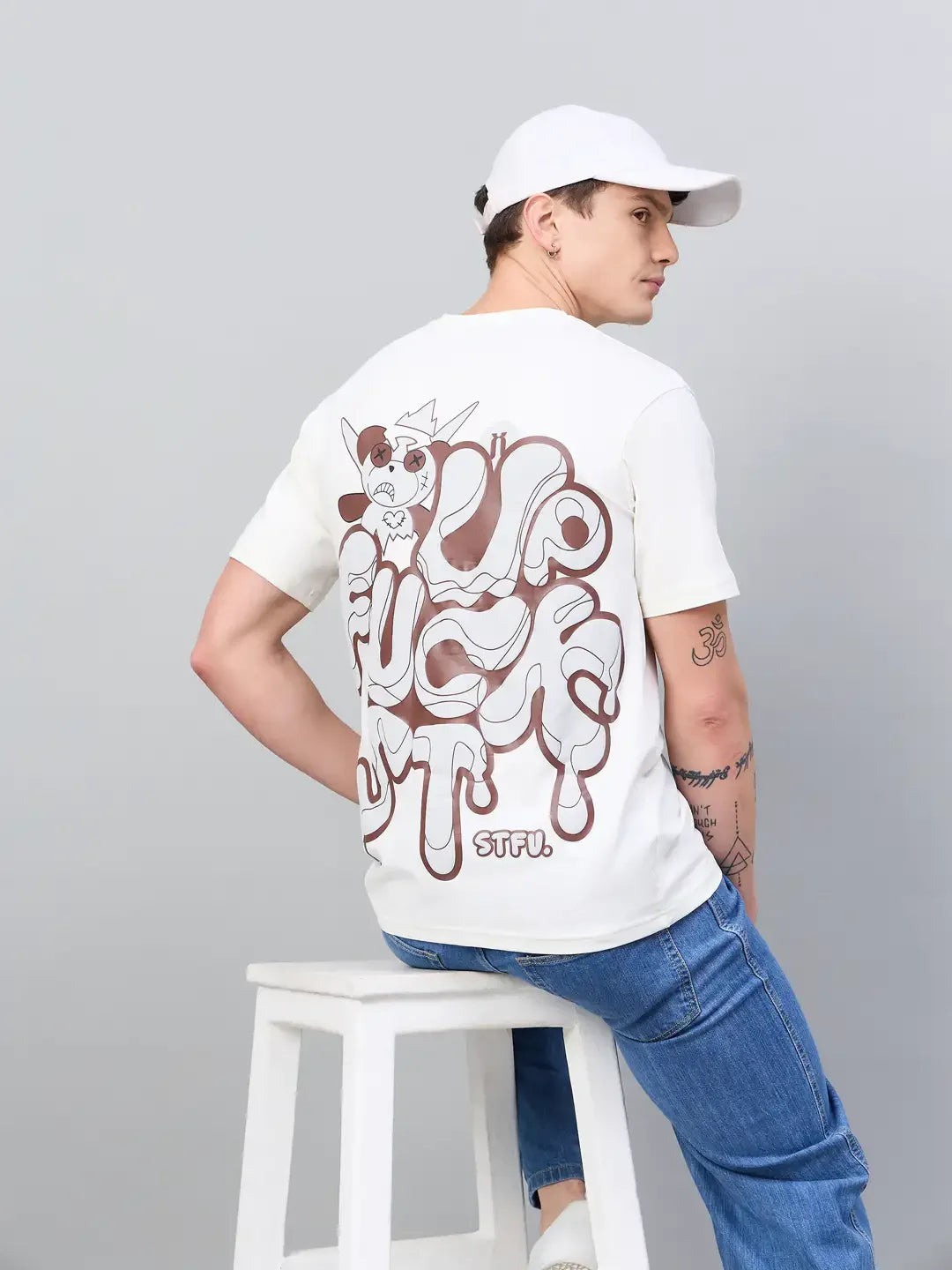 Model wears 98degreenorth Men Typography Oversized Offwhite Printed Round Neck T-shirt, seated against a gray background.