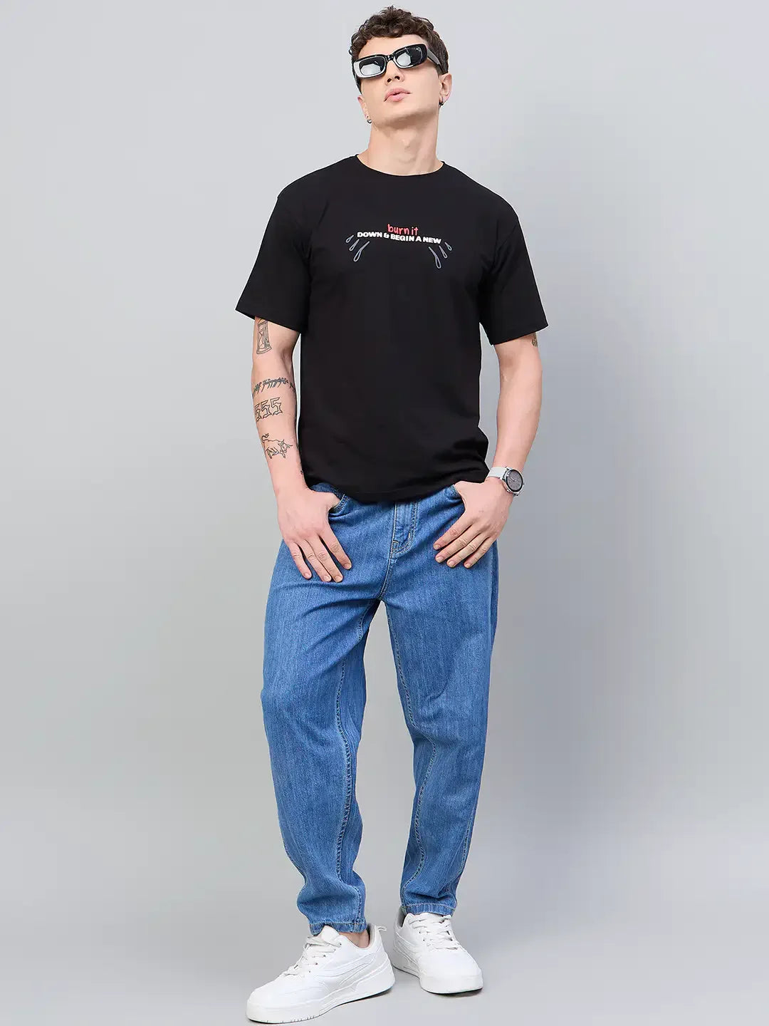 Man in sunglasses wears a 98degreenorth Men Typography Printed Black Round Neck T-shirt, blue jeans, and white sneakers.