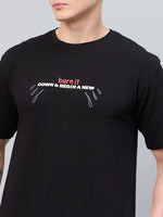 A person wears the 98degreenorth Men Typography Printed Black Round Neck T-shirt with bold text and teardrop graphics.