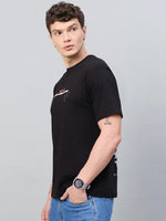 A man in a 98degreenorth Men Typography Printed Black Round Neck T-shirt and blue jeans stands sideways, looking left.