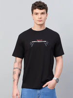 Man in a 98degreenorth Men Typography Printed Black Round Neck T-shirt, blue jeans, tattoos, and a watch.