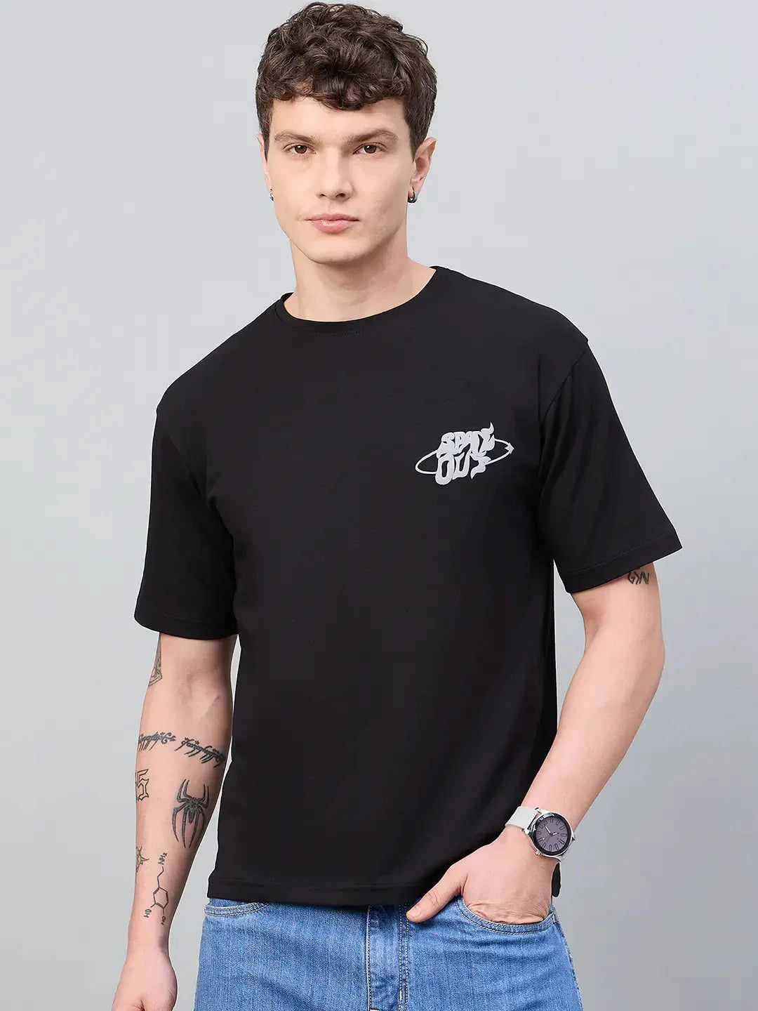 Man in 98degreenorth Men Typography Printed Round Neck Black T-shirt, blue jeans, and wristwatch, streetwear style.
