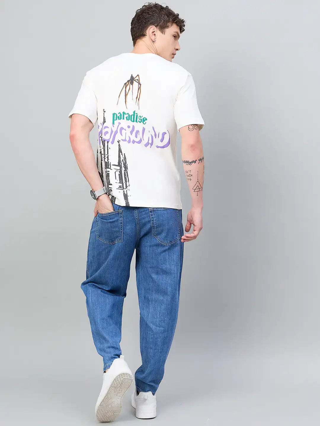 Man in a 98degreenorth Typography Printed Offwhite T-shirt stands with his back to the camera against a gray background.