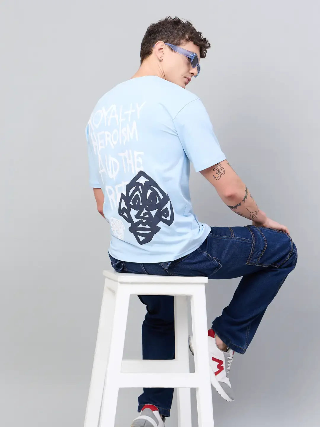 Man wears 98degreenorth Men Typography Printed Sky Round Neck T-shirt with jeans and sneakers, seated for a street style look.