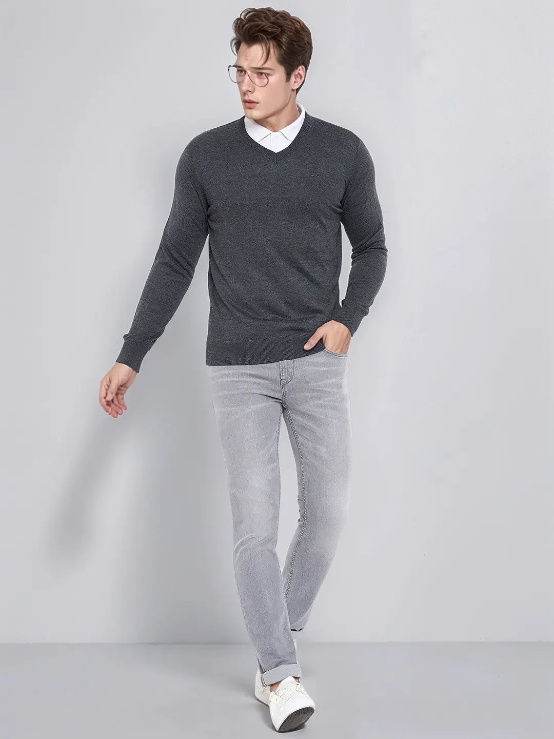 A man in glasses wears a 98degreenorth Men’s Anthra Merino Wool V-Neck Sweater with a white shirt and gray jeans indoors.